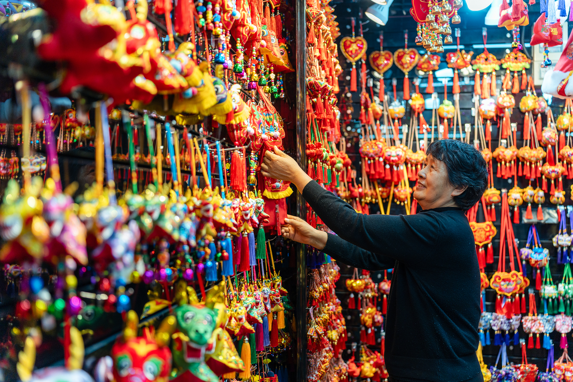 2023年12月11日，金華義烏國(guó)際商貿(mào)城，龍年喜慶用品掛滿(mǎn)攤位，顧客正在挑選中。